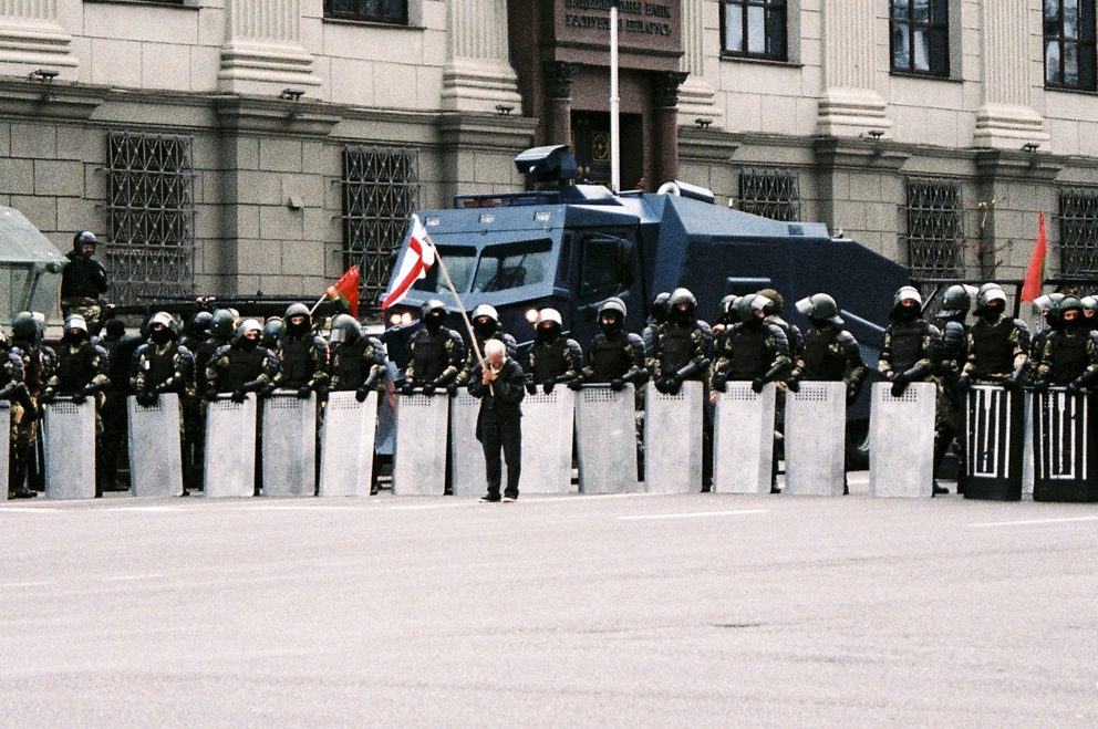 Bewaffnete Polizeikräfte in Belarus, davor ein Mann mit Belarus-Flagge.